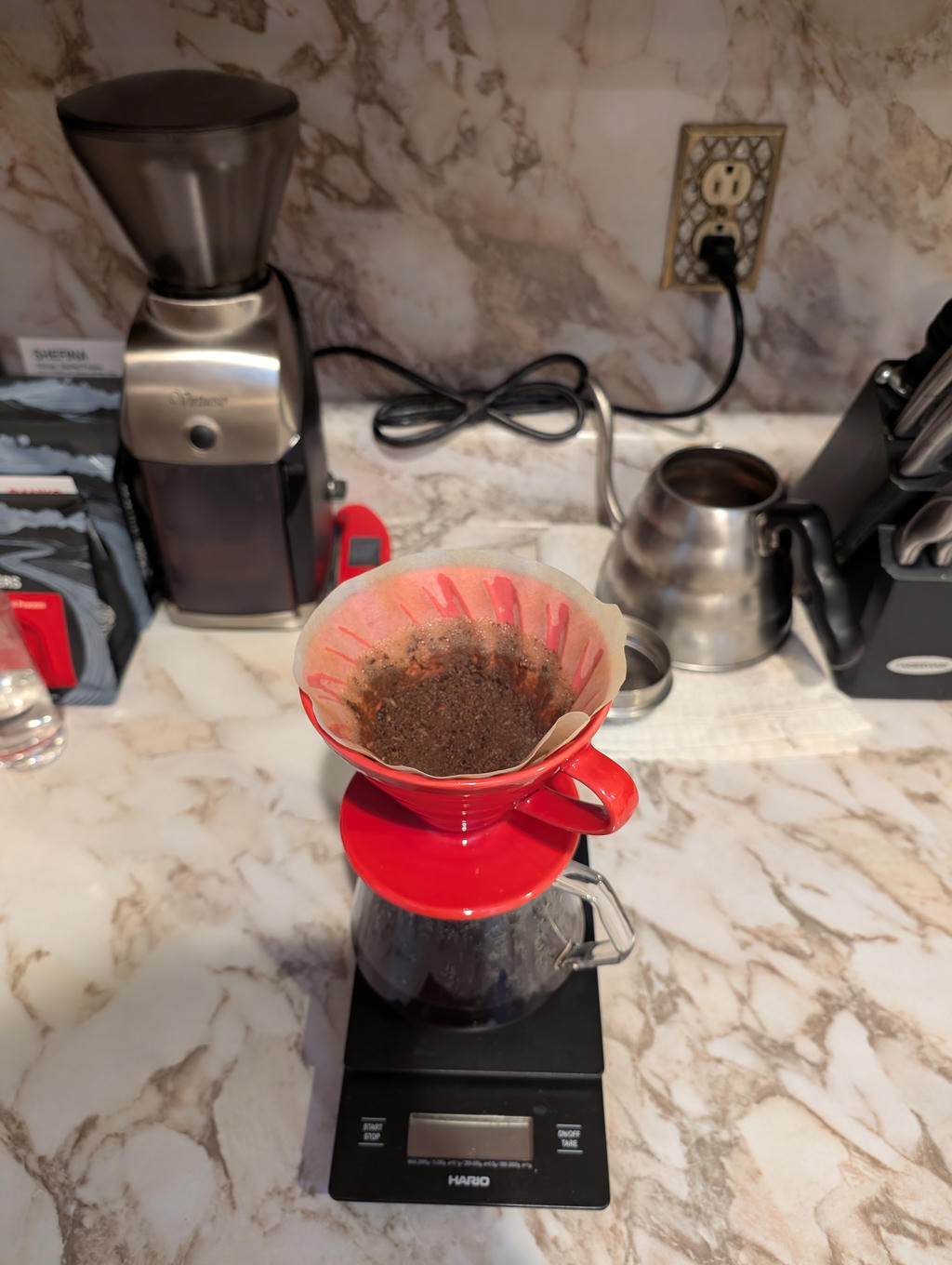 My coffee setup on the kitchen counter: a black Hario scale, with a red V60 pour over dripper holding a filter with coffee freshly brewed